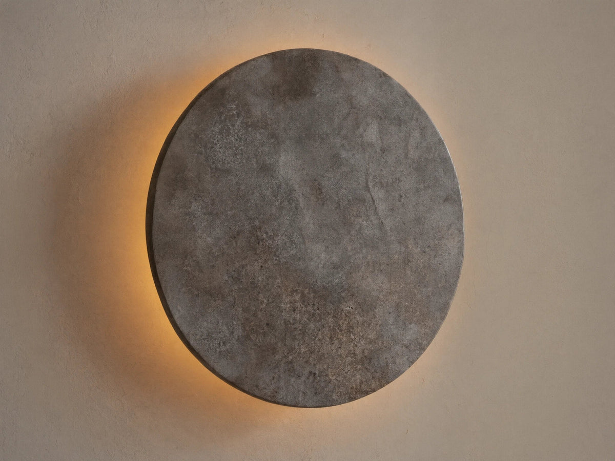 Odette Outdoor Sconce: Oval dark grey natural stone sconce on a beige wall, emitting warm golden LED light from behind.
