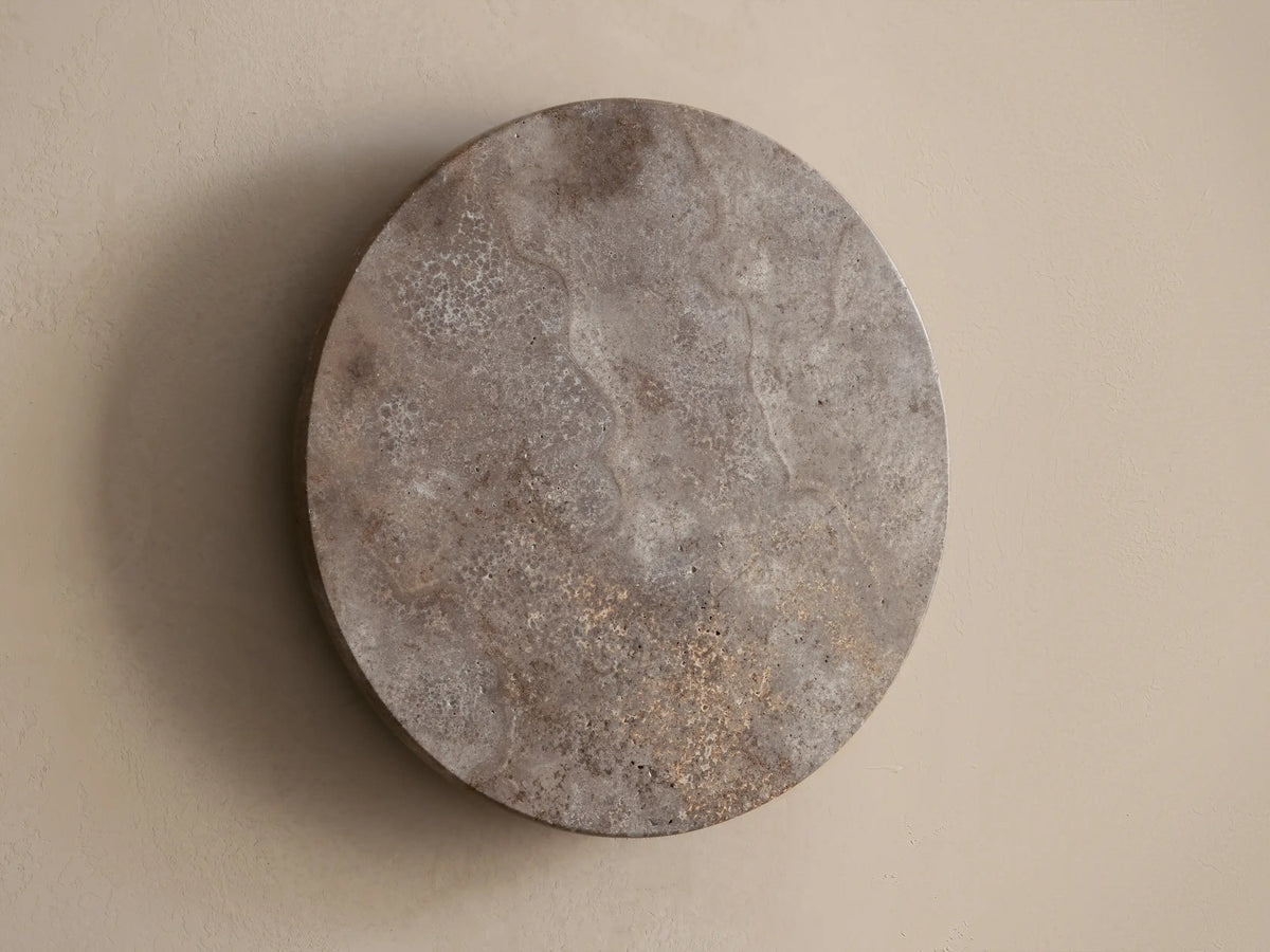 Odette Outdoor Sconce: Oval dark grey natural stone sconce on a beige wall, emitting warm golden LED light from behind.