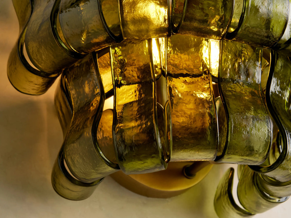 Ghiaccio Sconce featuring wavy, olive green curved glass panels layered on a neutral wall, next to a brown-framed mirror.