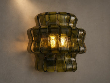 Ghiaccio Sconce: Dark green wavy textured glass wall sconce, glowing warmly, mounted on a light-colored wall.