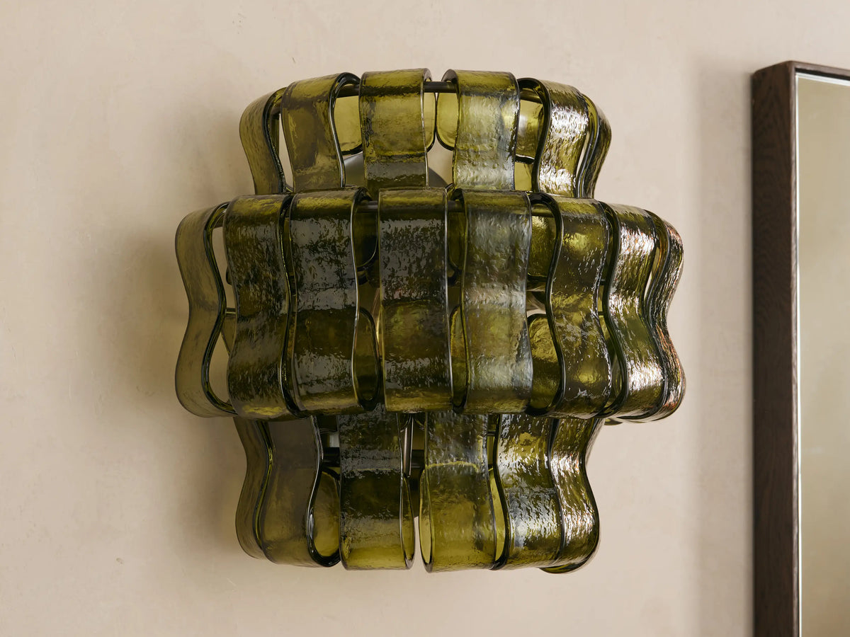 Ghiaccio Sconce: Dark green wavy textured glass wall sconce, glowing warmly, mounted on a light-colored wall.