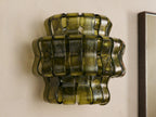 Ghiaccio Sconce: Dark green wavy textured glass wall sconce, glowing warmly, mounted on a light-colored wall.