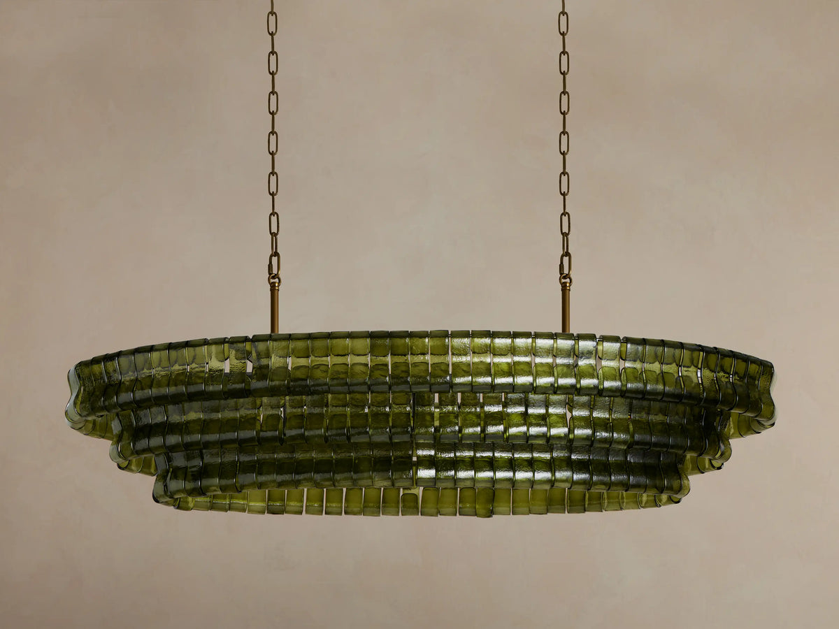 Illuminated Ghiaccio Oval Chandelier with multi-tiered olive green rectangular glass pieces, emitting a warm glow, hanging from chains.