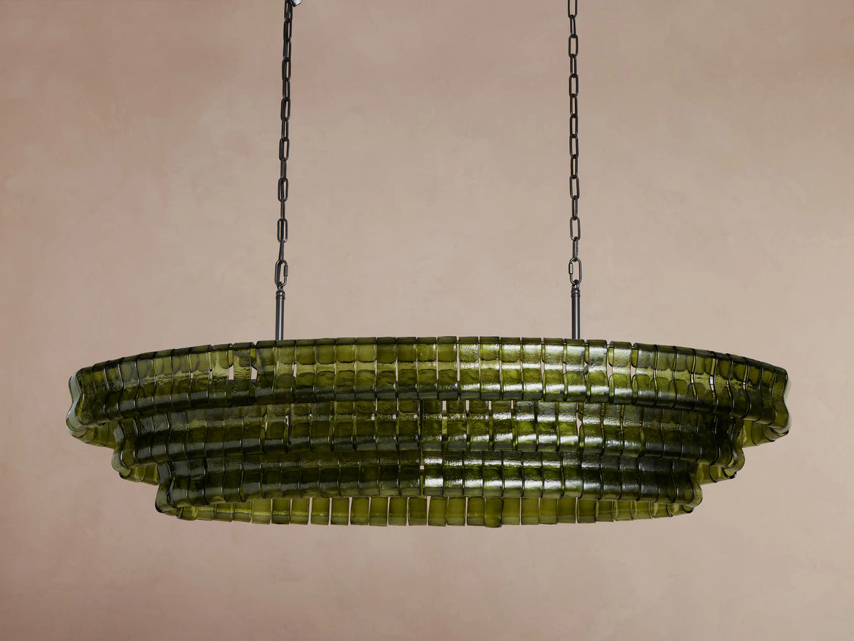 Ghiaccio Oval Chandelier, olive green curved glass squares in a tiered oval design, illuminated brightly, hanging from dark chains.