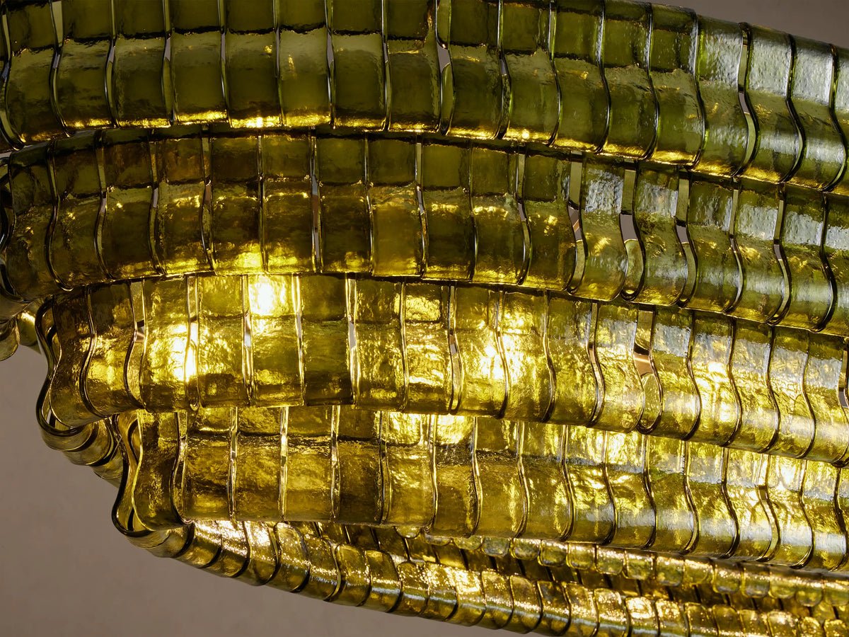 Oval Ghiaccio Chandelier, with stacked layers of textured green glass pieces, suspended by two dark chains against a light wall.