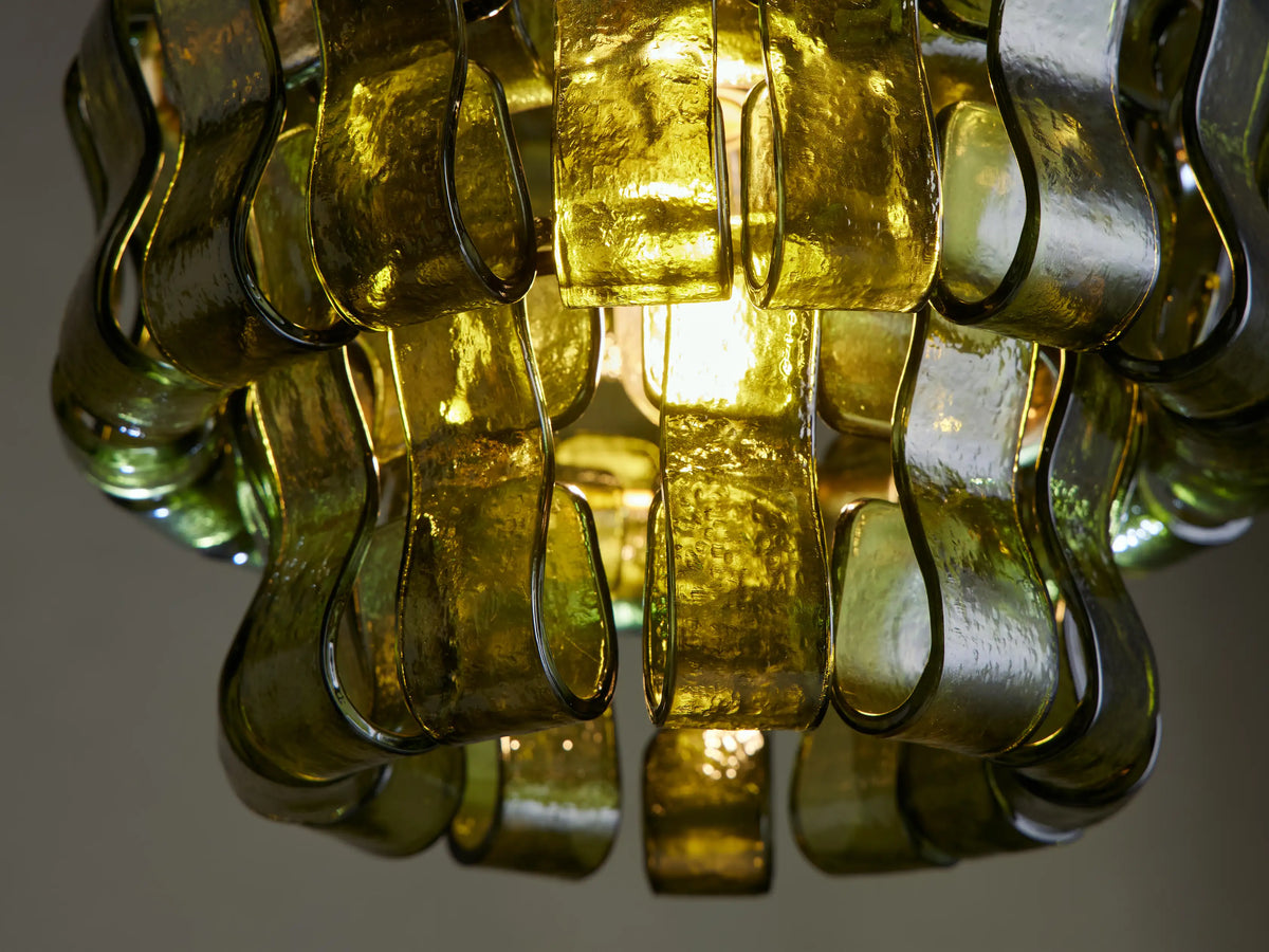 Ghiaccio Pendant with layered, wavy green curved glass panels suspended by a brass rod & chain against a neutral background.