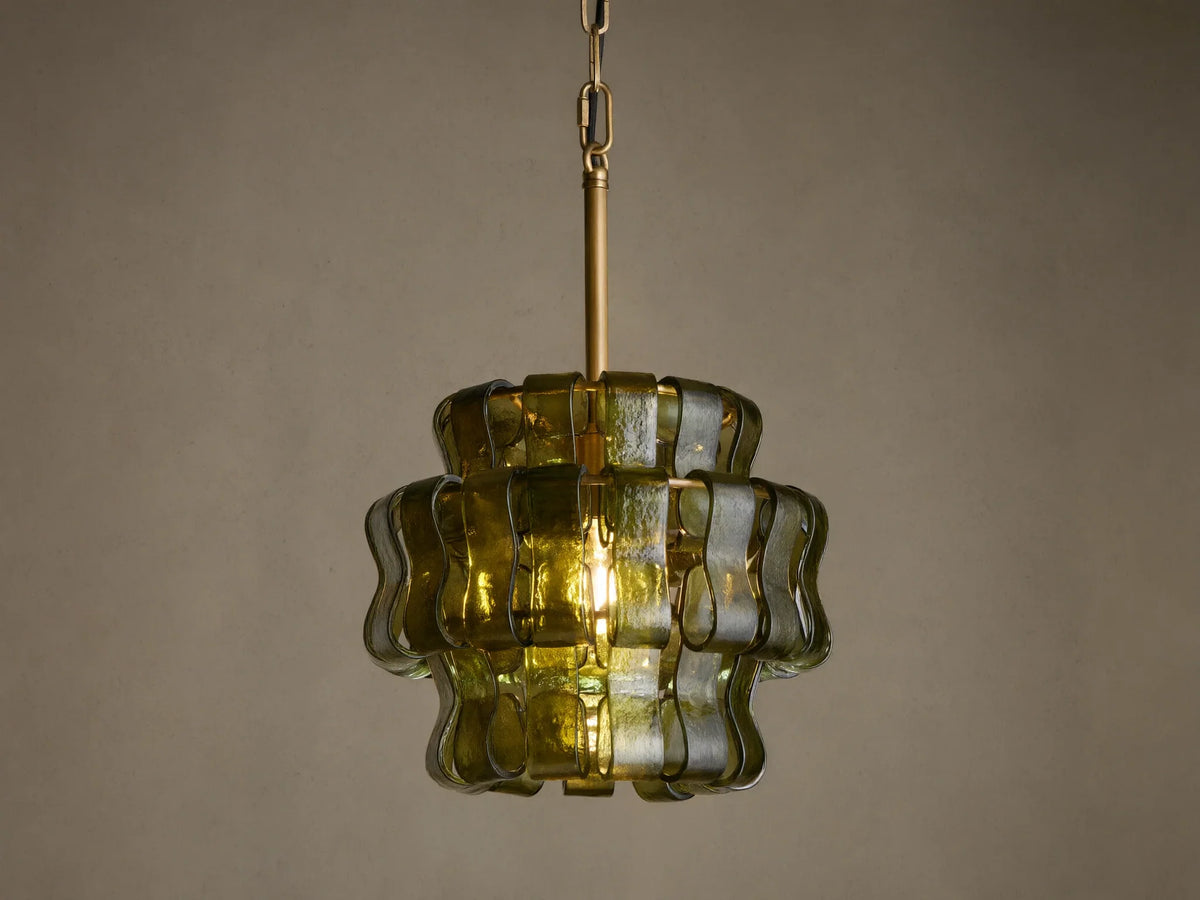 Ghiaccio Pendant, a tiered dark green wavy curved glass pendant light with brass chain, glowing warmly against a neutral wall.