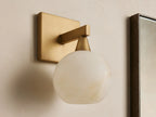 Front view of a brass wall light with a square backplate, horizontal arm, and glowing, translucent white veined globe shade.
