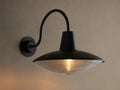 Close-up of Bennett Outdoor Sconce, black wall-mounted with a curved arm. Ribbed clear glass diffuser glows with warm light.