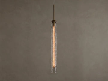 Vertical view of a lit pendant light with a clear textured glass cylinder, a warm filament bulb, and a brass-colored top fixture.