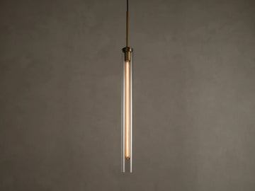 Front view of a modern brass and clear glass pendant light fixture with a long, illuminated filament bulb inside.