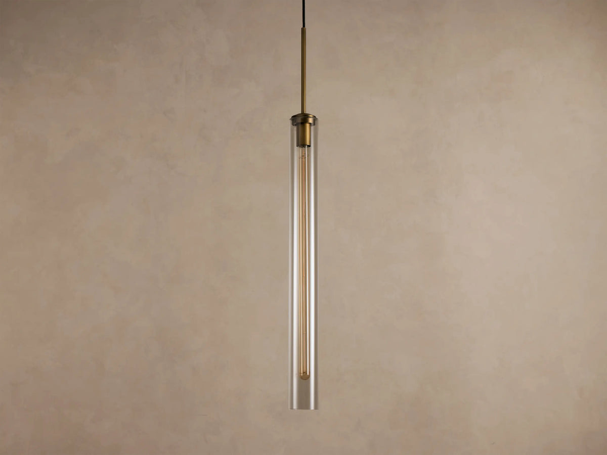 Brass and clear glass cylindrical pendant light with an exposed filament bulb, hanging vertically.