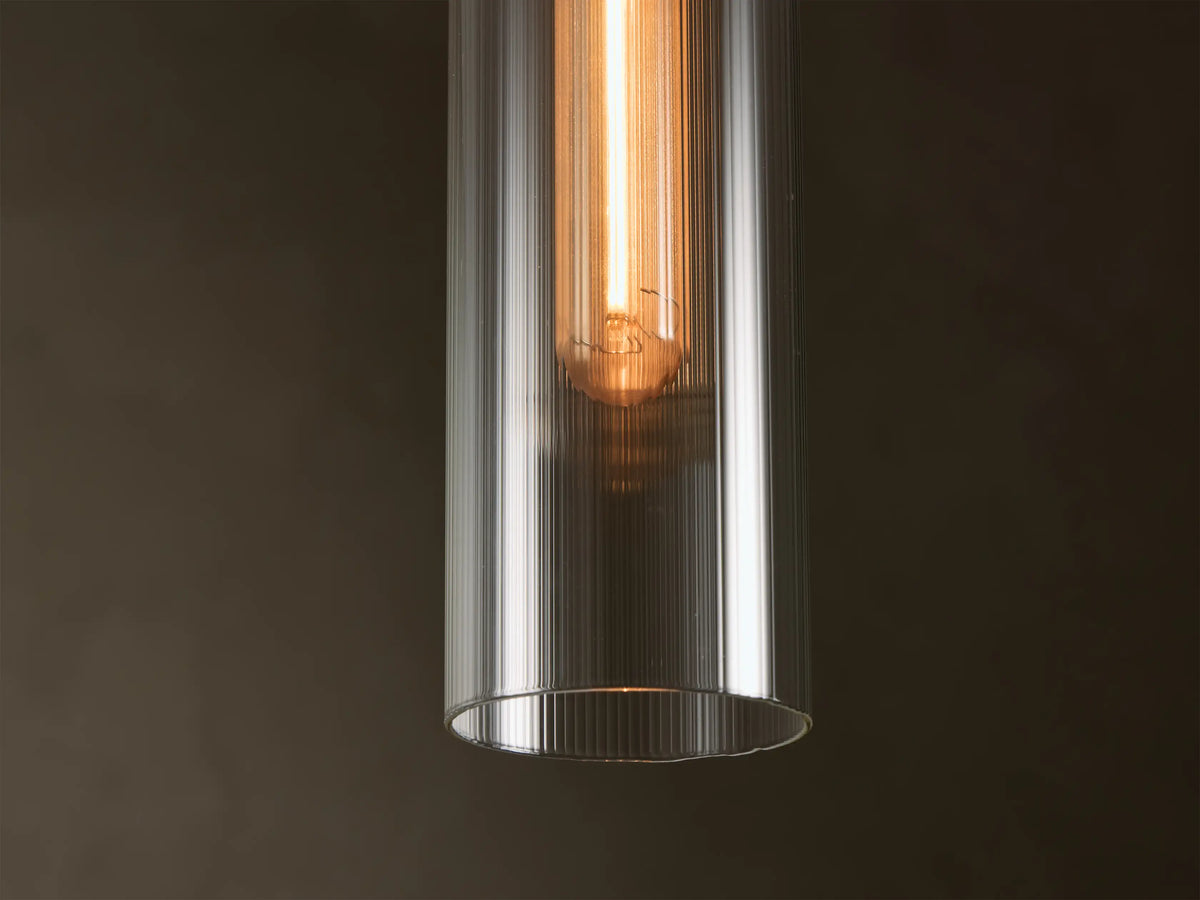 Close-up of a clear ribbed glass Pendant Light with a warm glowing Edison-style bulb inside.