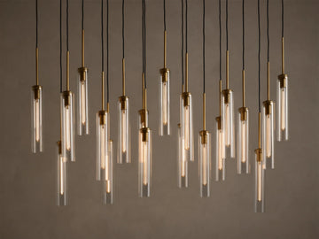 Multiple illuminated pendant lights with clear glass tubes and brass fixtures, hanging at varying heights from black cords.