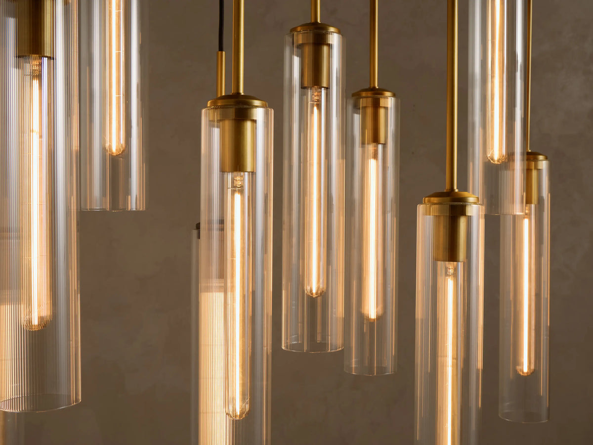 Multiple modern pendant lights with clear glass cylinder shades, brass accents, and black cords, hanging at varying heights.