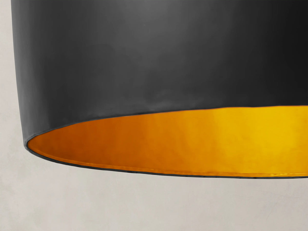 Fria Cone Pendant, a matte black inverted cone-shaped iron pendant light with a brass interior, hanging from a chain.