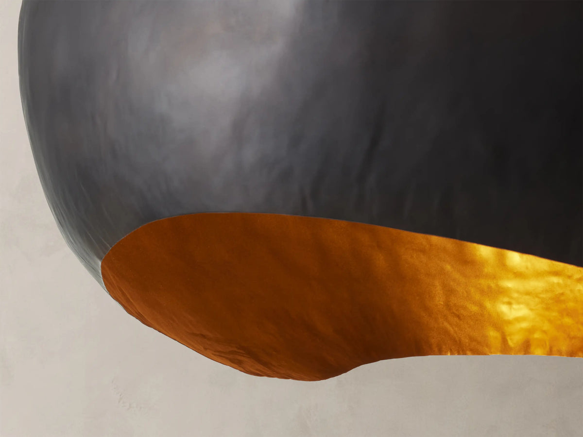 Front view of the Fria Dome Pendant, with its dark, organic-shaped iron exterior and warm, reflective brass interior.