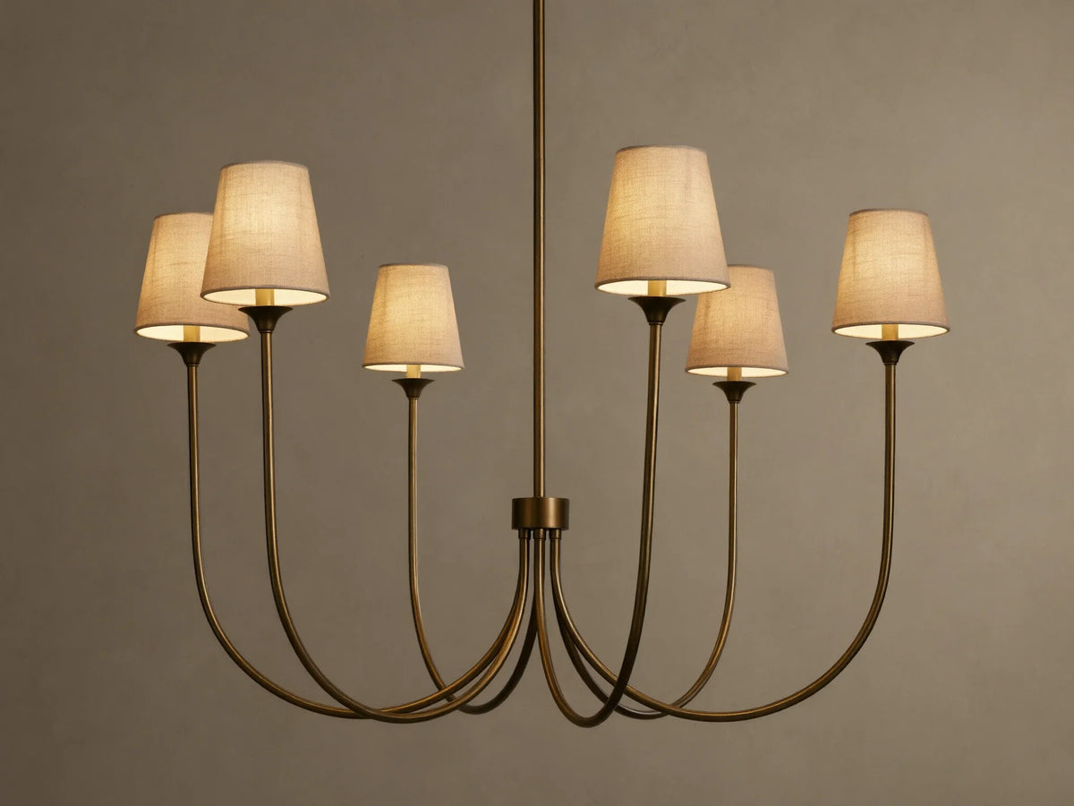 Saige Round Chandelier with a bronze finish, six illuminated off-white tapered fabric shades, hanging against a dark background.