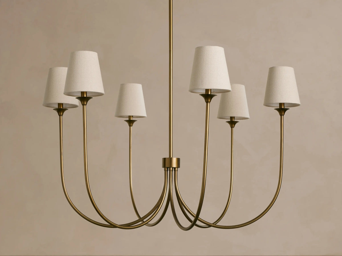 Saige Round Chandelier: Brass finish, six elegantly curved arms holding off-white tapered fabric shades, hanging.