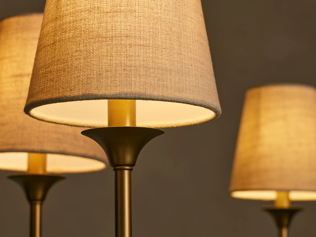 Close-up of Saige Round Chandelier's bronze arms & illuminated off-white fabric shades. Warm glow on textured fabric.