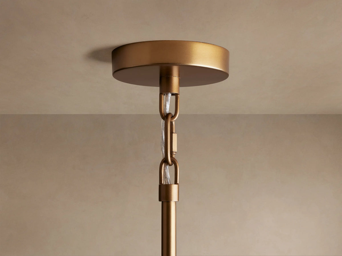 Saige Round Chandelier's brass ceiling mount with hanging chain & clear tubing for wires, against a beige ceiling.
