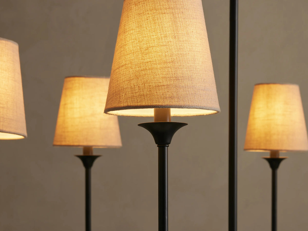 Close-up of Saige Round Chandelier with dark bronze metal arms and illuminated off-white tapered fabric shades, glowing warmly.