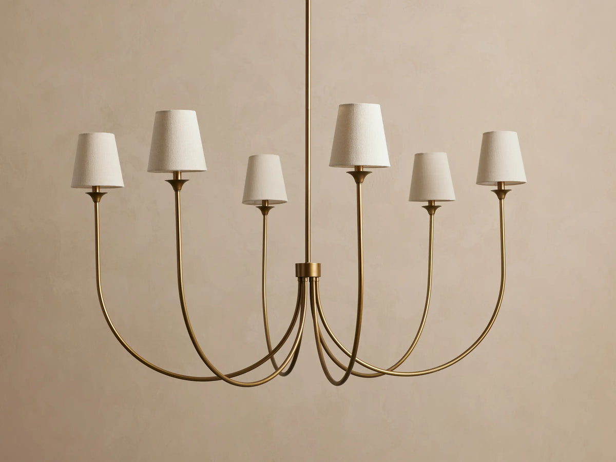 Saige Round Chandelier, brass-finished metal, with 6 elegantly curved arms, each topped with an off-white fabric shade.