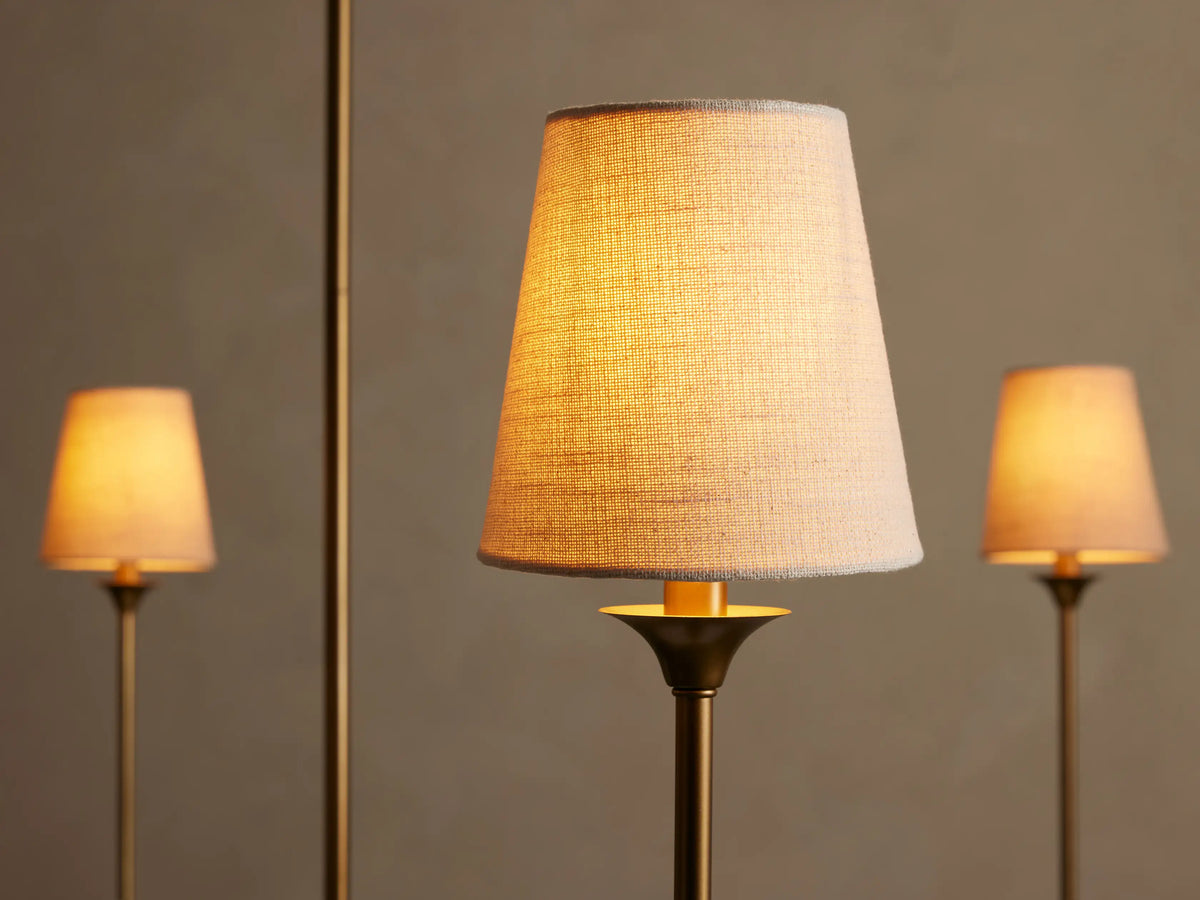 Close-up of a glowing off-white textured shade from the Saige Round Chandelier, mounted on a brass-finished arm.
