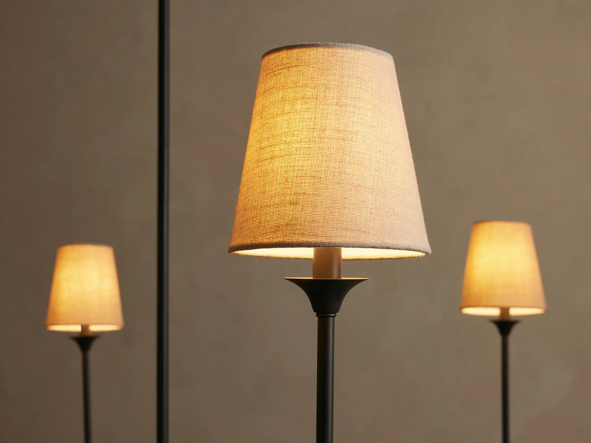 Saige Round Chandelier. Close-up of three arms with glowing off-white tapered fabric shades on dark metal stems.