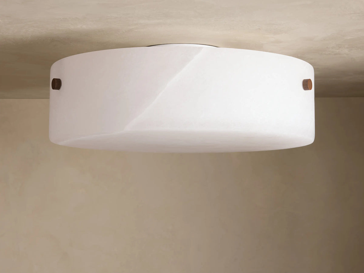 The Chayla Flushmount features a round alabaster shade with metal accents on a ceiling, casting soft ambient light.