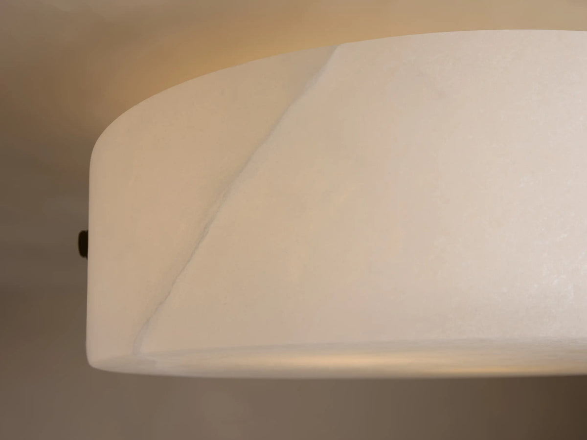 Chayla Flushmount with a smooth, rounded alabaster shade and dark metal accents mounted on a light-colored ceiling.