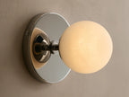 Wall-mounted light fixture with a round white glass globe and a metallic backplate. Mounted on a beige textured wall.