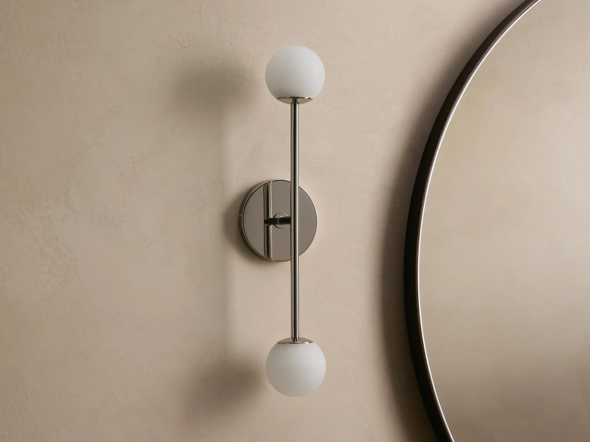 Wall-mounted lamp with a sleek metal fixture, featuring two spherical frosted glass bulbs, vertically aligned against a neutral wall.