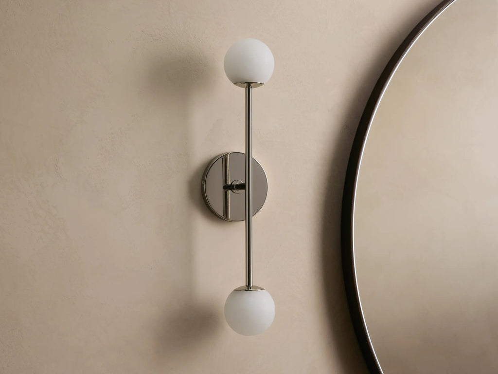 Wall-mounted lamp with a sleek metal fixture, featuring two spherical frosted glass bulbs, vertically aligned against a neutral wall.