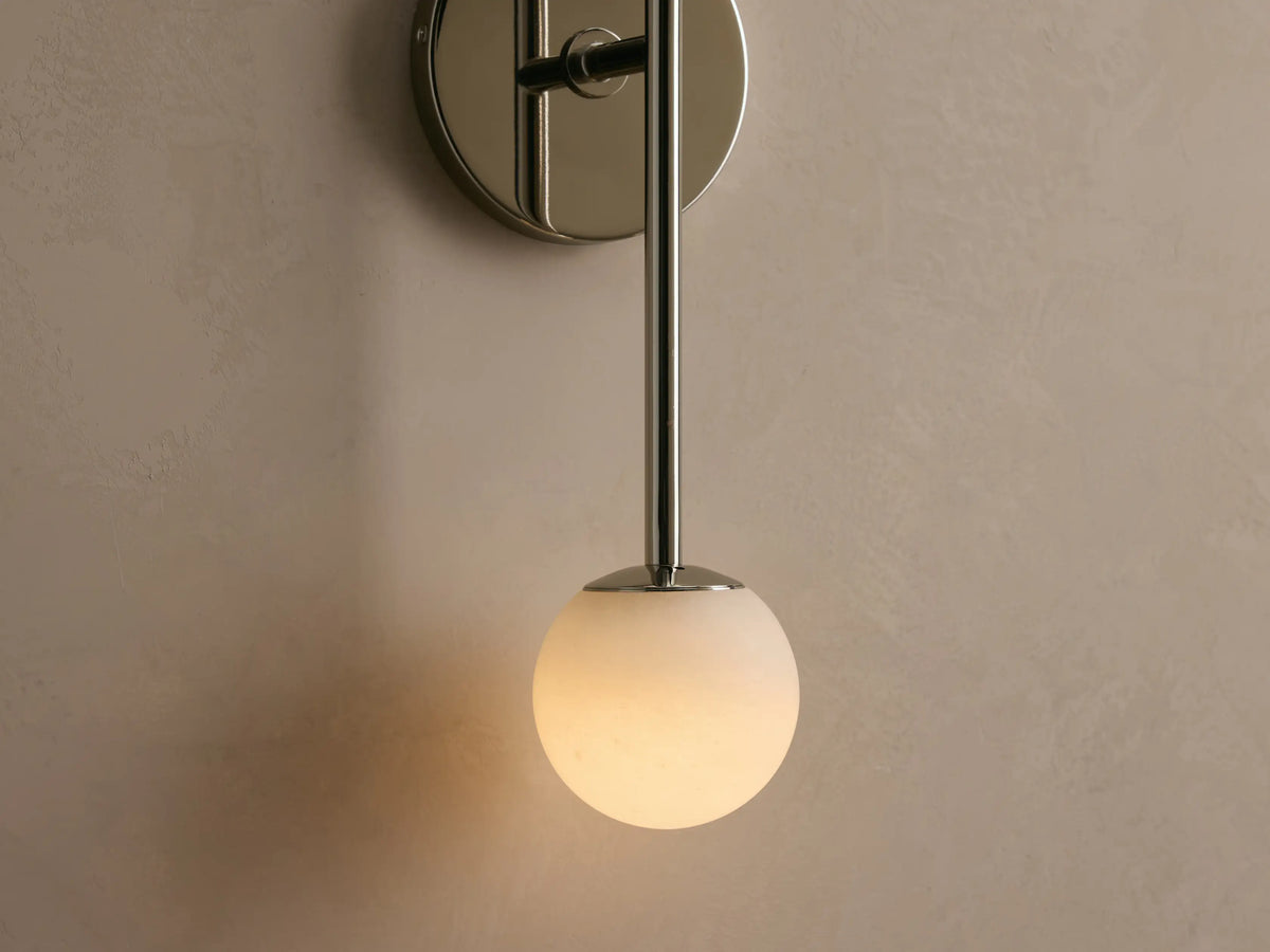 Wall-mounted light fixture with chrome finish and two frosted glass globes, vertically aligned on a beige wall next to a round mirror edge.