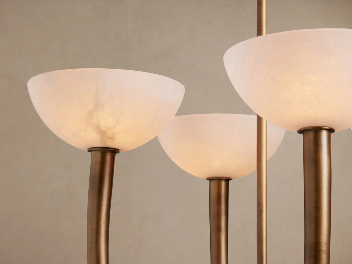Saguaro Chandelier: four white alabaster bowl shades and curved antique brass arms against a beige wall.