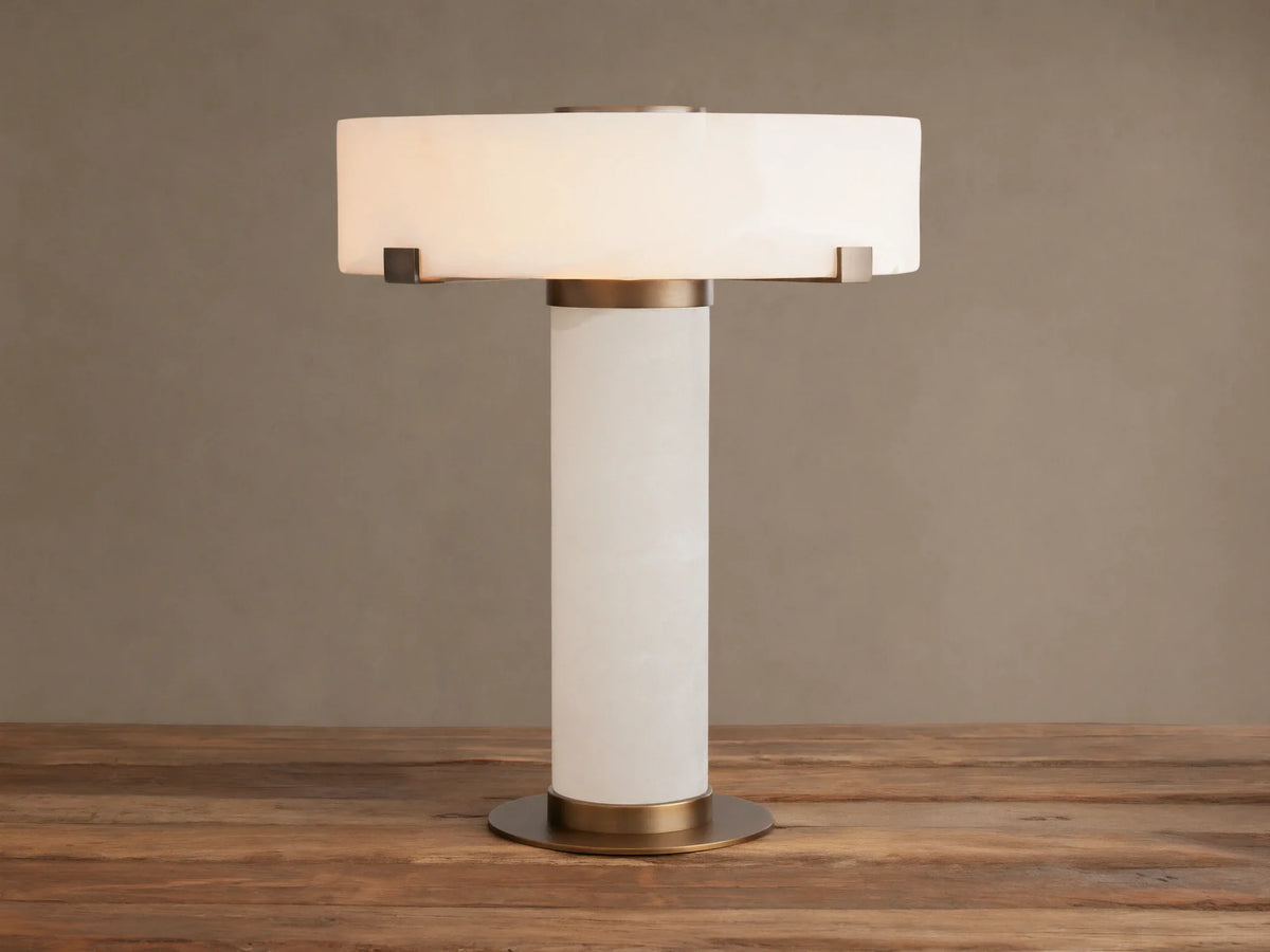 Chayla Table Lamp with glowing white alabaster shade, cylindrical alabaster base, and antique brass accents on a wooden table.
