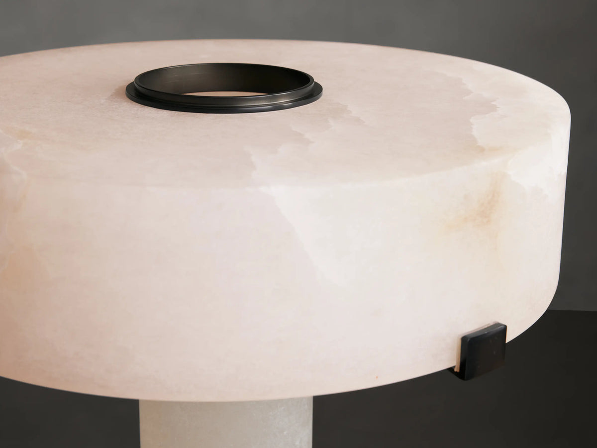 Chayla Table Lamp with natural alabaster cylinder base, bronze accents, wide alabaster shade on wooden surface, simple background.