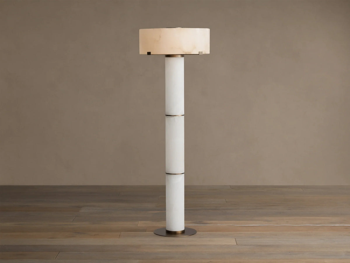 Chayla Floor Lamp: Tall, segmented white alabaster column, glowing cylindrical shade with natural patterns, antique brass accents, wood floor.