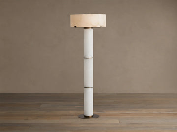 Chayla Floor Lamp: Tall, segmented white alabaster column, glowing cylindrical shade with natural patterns, antique brass accents, wood floor.