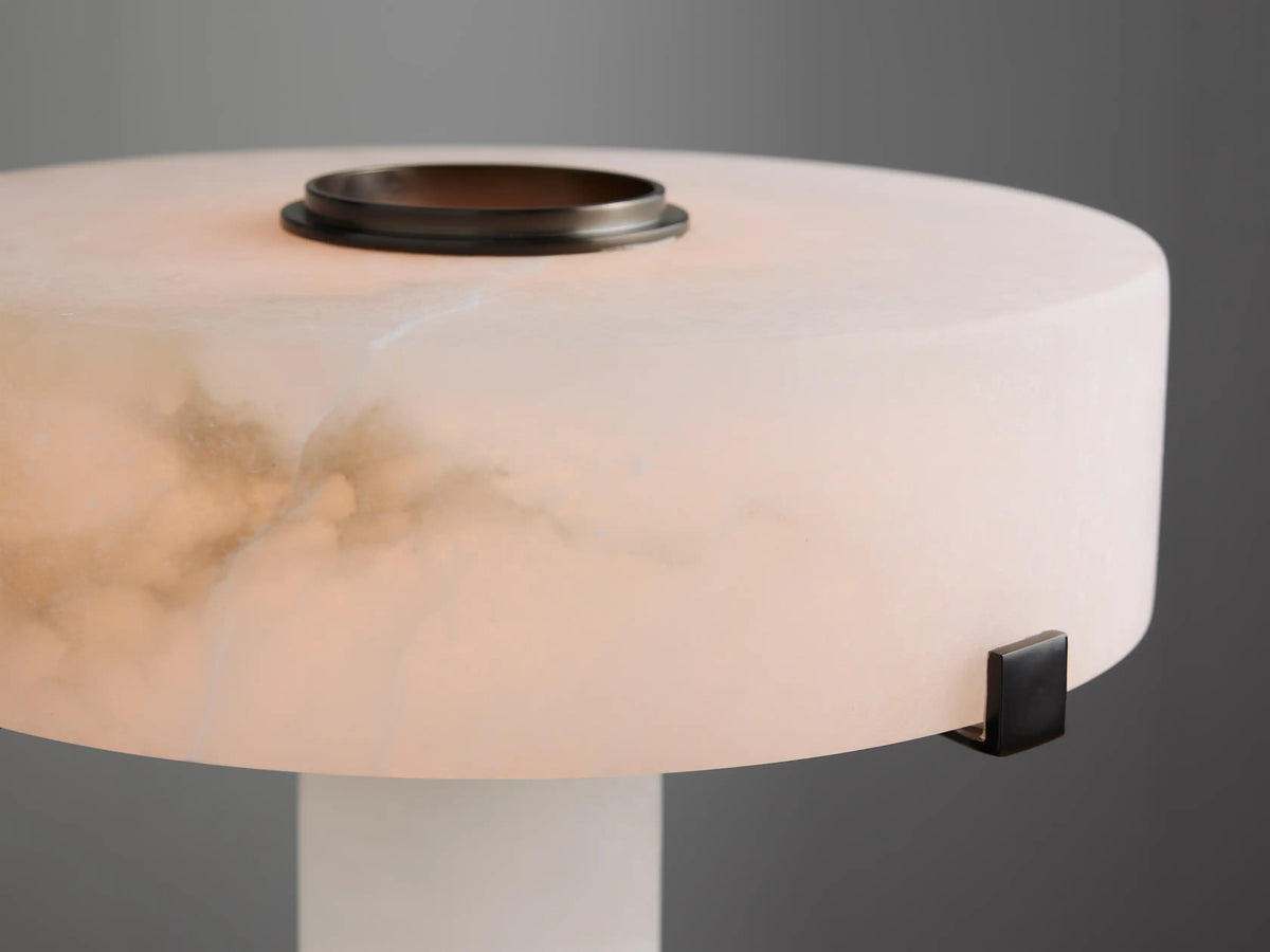 Chayla Table Lamp in Bronze. White alabaster cylindrical base & shade with natural tan veining, bronze accents on a wooden table.