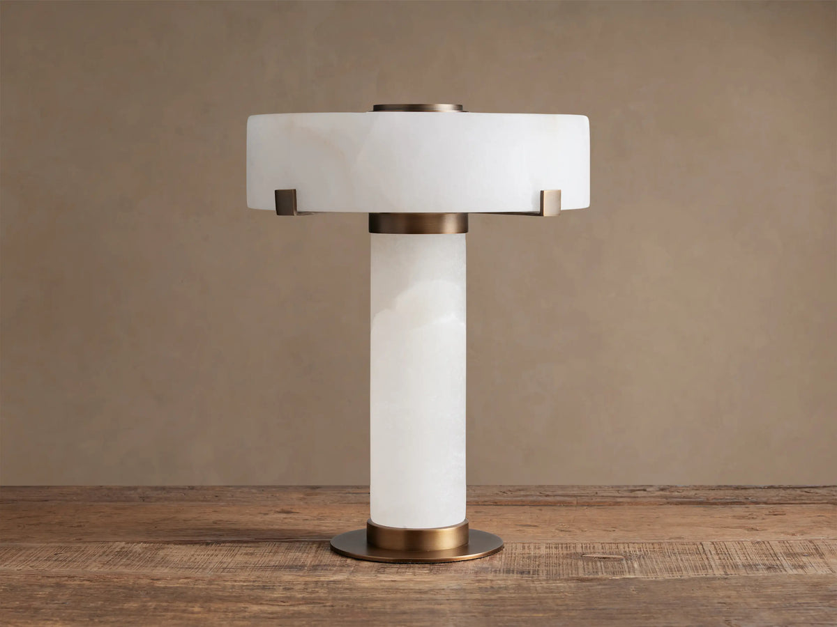 Chayla Table Lamp: white alabaster cylindrical body, drum shade, antique brass accents, on wooden table.