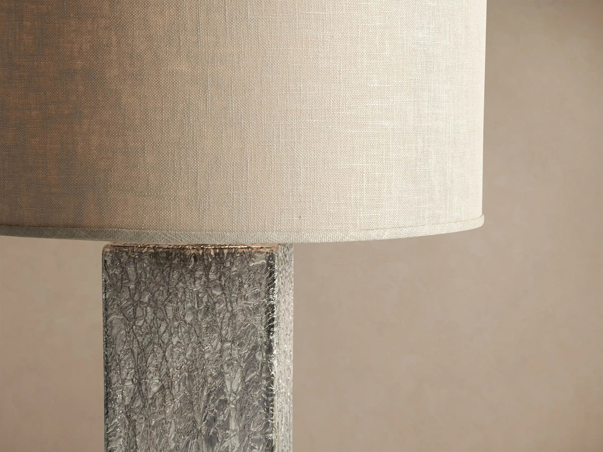 Adrano Table Lamp featuring a rectangular, textured fused silver cast glass base and a natural linen drum shade on wood.