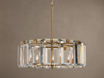 Round Amaya Chandelier with brass frame & thick, clear crystal panels, showcasing five candelabra bulbs, against a plain wall.