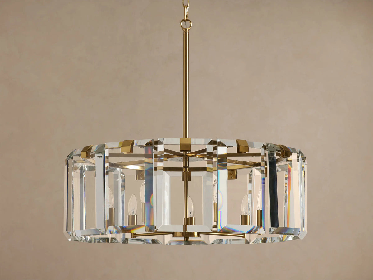 Amaya Round Chandelier, featuring a round, faceted clear crystal drum with a brass-plated frame, unlit candelabra bulbs inside.