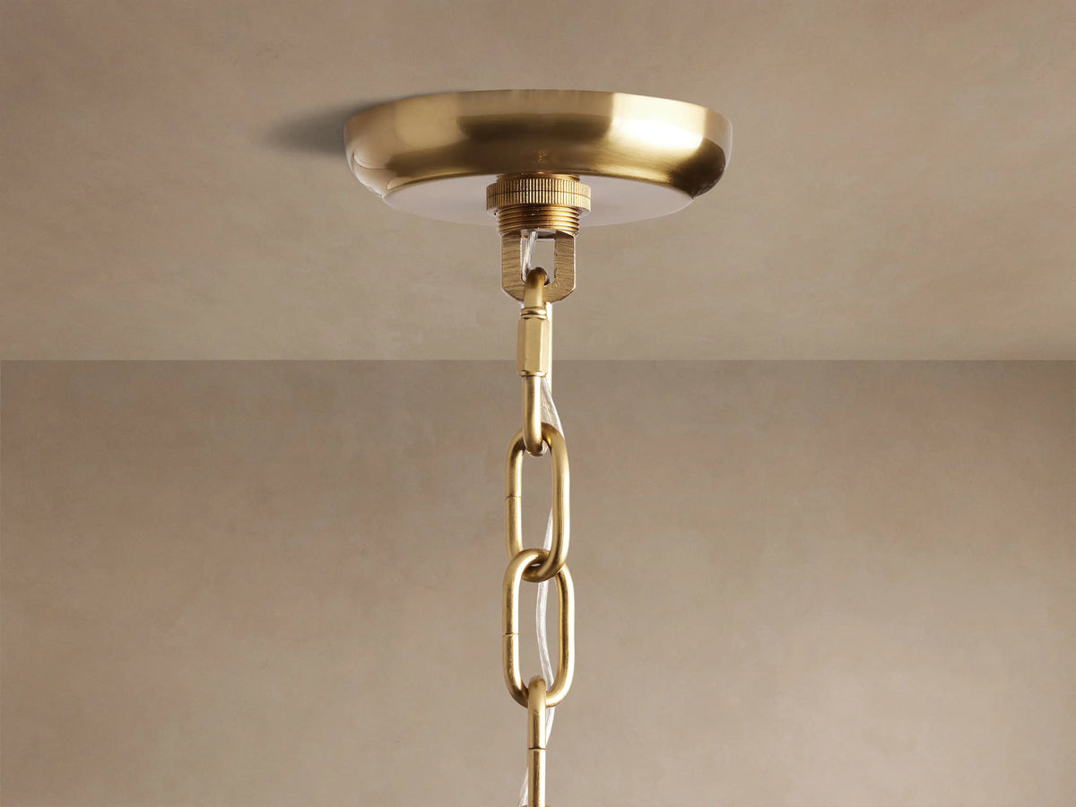 Close-up of Amaya Round Chandelier's brass-plated canopy mounted on a beige ceiling, with a brass chain and clear wire.