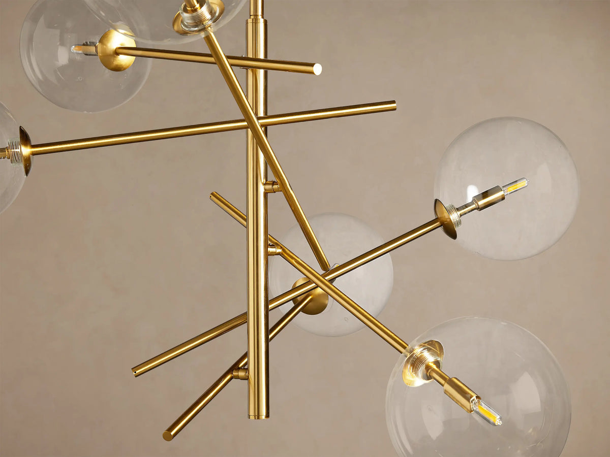 Roscoe Chandelier: modern plated brass fixture with multiple arms radiating out, holding clear glass globes with illuminated bulbs.