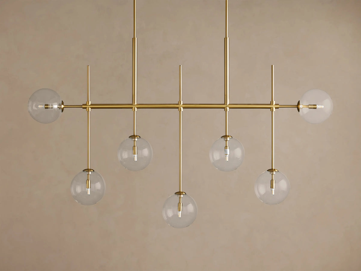 Roscoe Linear Chandelier: Brass-finished linear frame with 7 clear glass globes containing bulbs, 5 hanging, 2 horizontal.