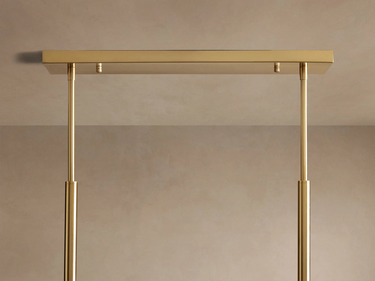 Roscoe Linear Chandelier. Close-up of the rectangular golden brass canopy with two sleek support rods against a neutral wall.