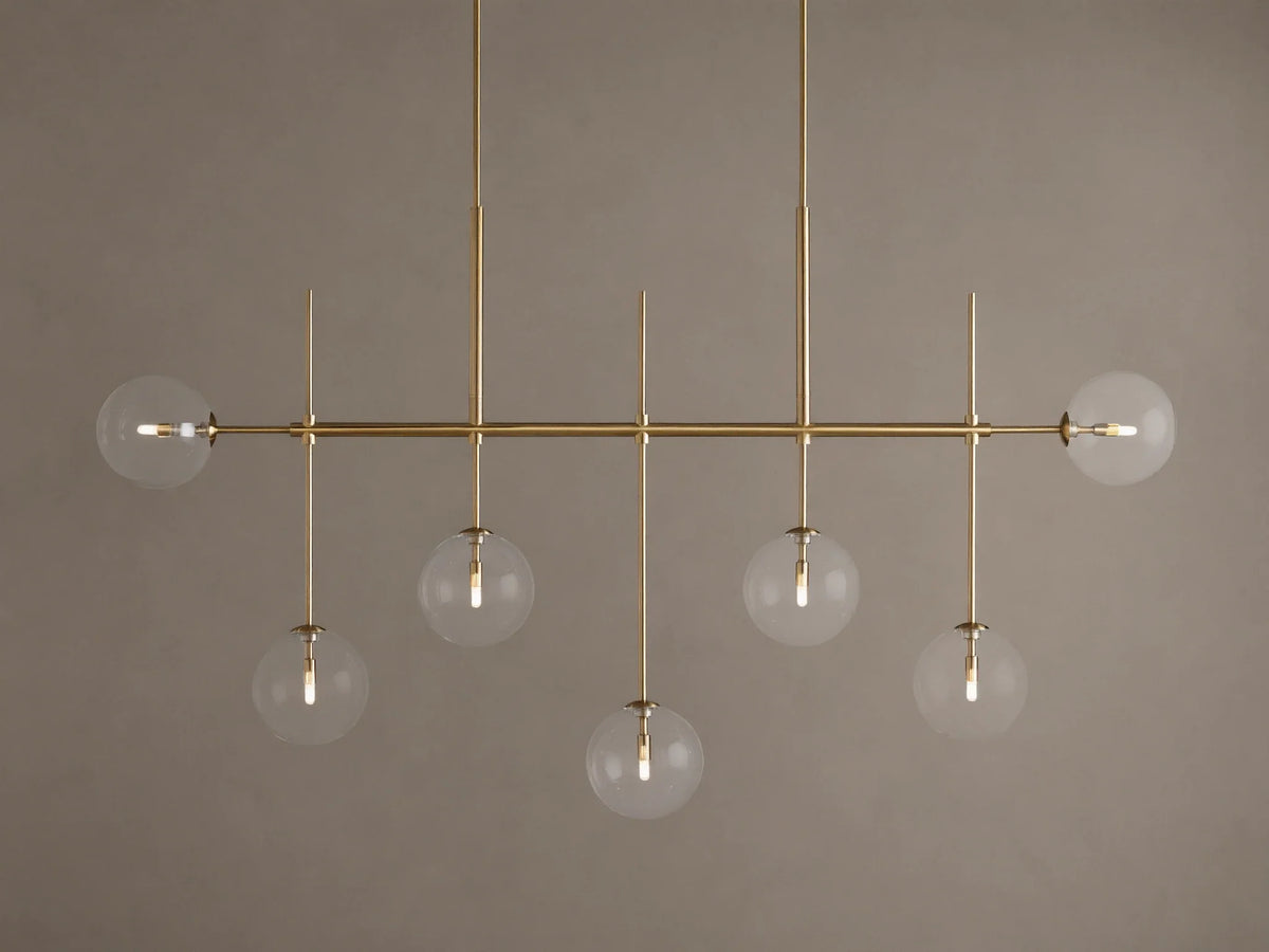 Roscoe Linear Chandelier: 7 illuminated clear glass globe lights on a brass-finished horizontal bar. Angled view.